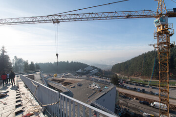 The exterior of a business building under construction is surrounded by trucks, cranes, and various construction materials, creating a bustling scene of an expansive industrial worksite in progress