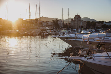 Calm marina view during sunset in Greece, with yachts and sailboats reflecting golden light on still water.