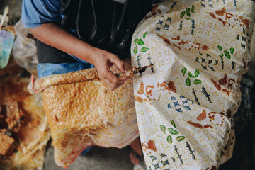 Person's hand is tracing design the pattern of batik tulis cloth using Canting.