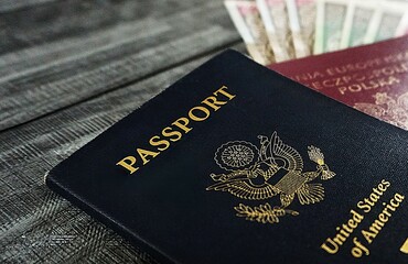 Zbliżenie na amerykański paszport. W tle widać inny paszport i pieniądze.