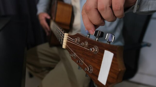 Close up hands of a man who tunes an acoustic guitar to start playing music. He twists the peg winder to adjust the sound. Composing music, learning to play acoustic guitar.
