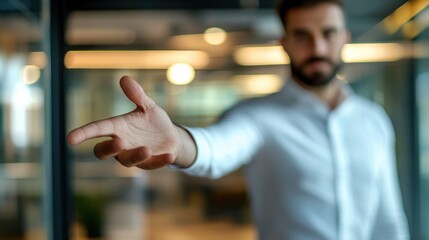 A man in white shirt extends his hand in a gesture of wanting to help or assist, blurred focus on his hand and body, modern office interior with glass walls
