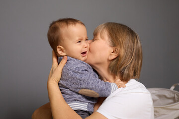 A grandmother embraces her upset grandchild, showering him with affection in a warm and comforting indoor environment while he cries softly