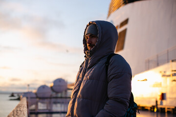 Portrait of a handsome man wearing warm puffer jacket and a hood standing  on a sun deck of a...
