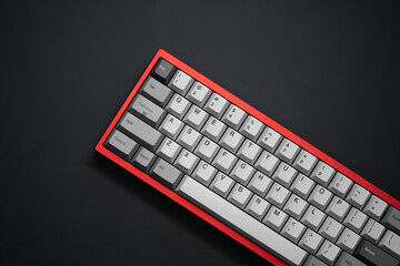 Close-up top view of a red mechanical keyboard with greyscale keycaps, captured in a flat lay style. Positioned in the bottom-right corner of the frame, partially cropped, on a matte black surface.