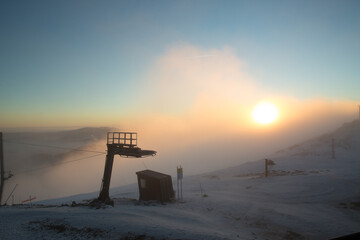 A breathtaking sunrise over a snowy mountain peak, partially covered by fog and mist.