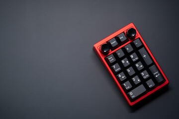 Numpad mechanical keyboard in vibrant red with white on black keycaps, featuring a sleek rotary knob at the top. Top view. Positioned in the lower right corner on a matte black surface.