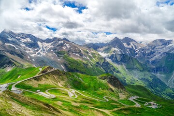 A winding road in Kaprun, Austria, offers stunning views of green mountains and snow-capped peaks. It is a popular route for both cyclists and drivers, surrounded by beautiful nature.