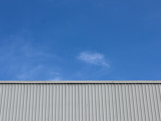Fototapeta premium Industrial factory building with aluminum metal texture on the exterior wall against the background of blue sky and clouds, modern architecture of corrugated steel facade. Copyspace, design.