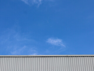Obraz premium Industrial factory building with aluminum metal texture on the exterior wall against the background of blue sky and clouds, modern architecture of corrugated steel facade. Copyspace, design.