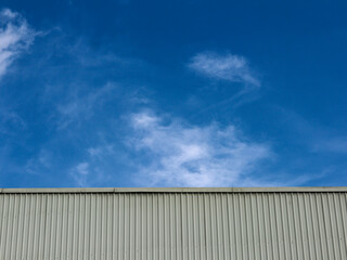 Fototapeta premium Industrial factory building with aluminum metal texture on the exterior wall against the background of blue sky and clouds, modern architecture of corrugated steel facade. Copyspace, design.