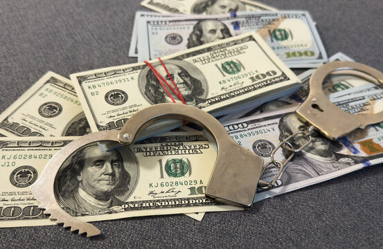 Financial crime, fraud, money laundering, corruption, or law enforcement : Bundles of US dollar 100 bills in a small case, alongside a pair of handcuffs placed over the US dollar currency.