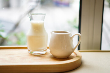 A glass jar of milk and a cup of espresso on a wooden tray with selective focused.