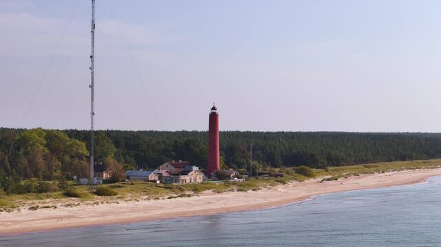 Drone fly low next to Lighthouse location, waterfront beach coastline of Latvia, aerial landscape view