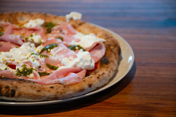 close-up of a plate of pizza baked in a wood-fired oven with a thick edge and toast with mortadella, mozzarella and angled pesto