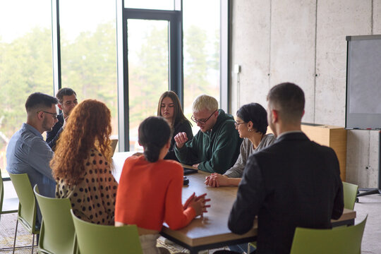 A young, diverse business team sitting together in a modern office, exchanging ideas and business plans, fostering collaboration and innovation for future success.