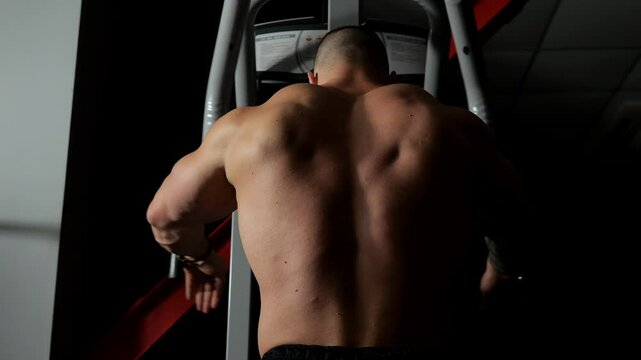 The silhouette of a muscular man with huge muscles performing strength exercises in the gym, he does exercises for the pectoral muscles on the pec deck simulator. Black background.