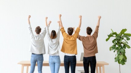 Fototapeta premium A group of four people celebrating with raised arms, standing in front of a table and a plant, conveying joy and teamwork.