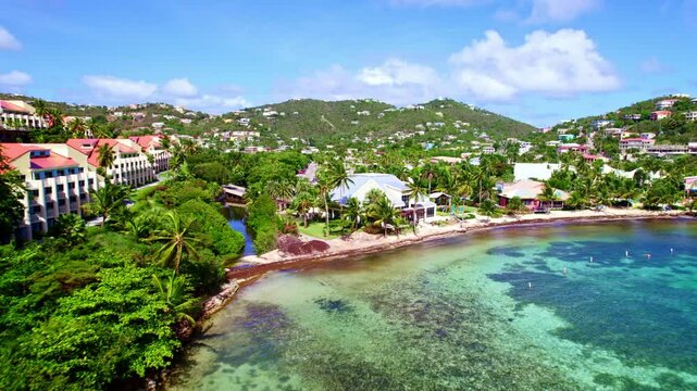 Aerial estabilshing to bay of St. Thomas, USVI, showcasing stunning beaches, lush hills, and crystal clear waters with hotels looking out to sea