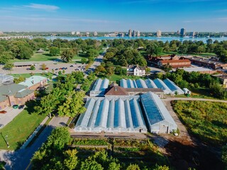 High angle view of a botanical garden with greenhouses, gardens, and city skyline. Urban parkland with rows of glasshouses. BELLE ISLE, DETROIT, MICHIGAN, UNITED STATES