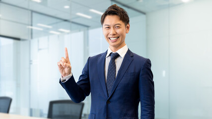 人差し指を立てて案内する笑顔の男性ビジネスマン