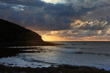 Dramatic sunset over rocky shore of Pacific Ocean near Raglan, New Zealand