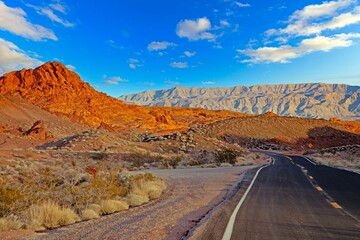 Desert road leading to rocky mountains under bright blue sky and sunny weather