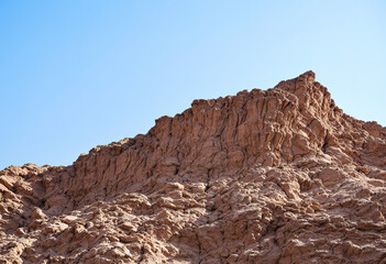 Fototapeta premium A close-up view of a rocky cliff face with intricate, layered patterns and textures, against a clear blue sky