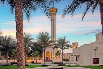 Islamic mosque with tall minaret framed by palm trees at sunset in peaceful courtyard