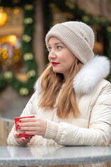 Portrait of a 30-35 year old woman against the background of a Christmas fair with a mug of hot drink in her hands