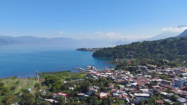Aerial view of a small town along Lago Atitlan coastline, surrounded by lush greenery, docks and vibrant blue waters. Panajachel, Guatemala.