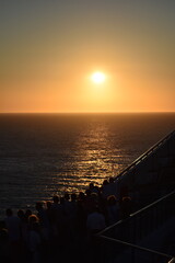 A beautiful sunset over the ocean with silhouettes of people on a ship's deck, the sun reflecting off the water, creating a serene and peaceful atmosphere at sea

