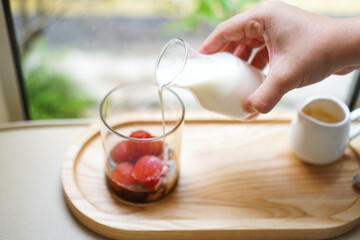A woman's hand pours milk into a glass filled with strawberry ice cubes and espresso to make a strawberry latte.