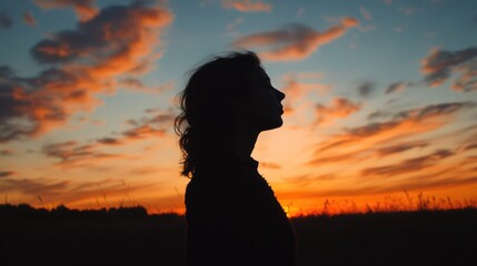 Fototapeta premium silhouette of a woman against a vibrant sunset sky with colorful clouds creating a serene and contemplative atmosphere