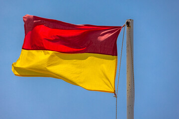 Red and yellow warning beach flag is under blue sky on a sunny day