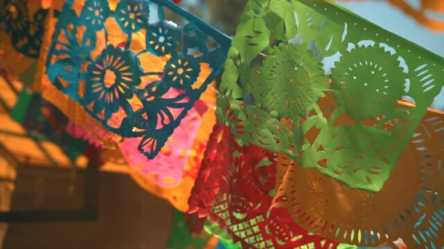 Traditional Mexican papel picado decorations with intricate designs and vibrant colors, static closeup with sunlight on windy day