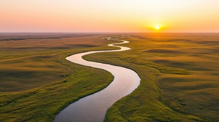 Winding river at sunset in vast grasslands landscape with golden horizon