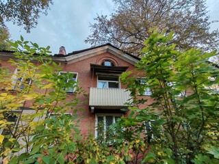 A vintage brick building with balconies and a gated entry, shaded by trees on a quiet street. The image conveys the timeless charm of urban housing, showcasing how older neighborhoods retain their