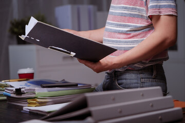 A man sits at his desk at home at night, working on his laptop. He views charts, checks documents,...