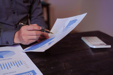A close-up of a male businessman at his desk, analyzing overtime graphs and business charts in a...