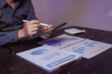 A close-up of a male businessman at his desk, analyzing overtime graphs and business charts in a...