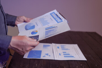 A close-up of a male businessman at his desk, analyzing overtime graphs and business charts in a...