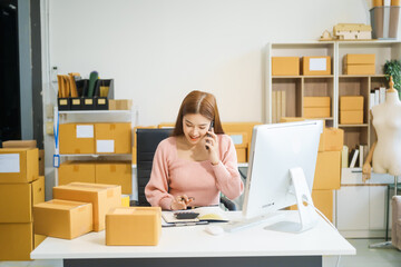 An Asian businesswoman sits at her desk, working on online sales and e-commerce marketing strategies. As a small business owner, she prepares and packages product boxes to ship to customers.