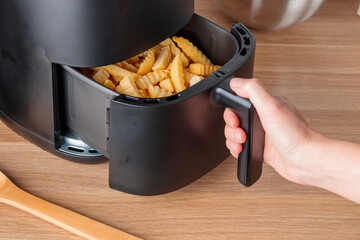 Woman at home using trendy kitchen gadget air fryer machine cooking deep-fried potato, small...