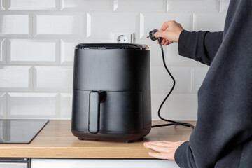 Woman at home using trendy kitchen gadget, air fryer, plugging in small convection oven on...