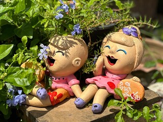 Two delightful clay dolls are sitting side by side on a wooden block