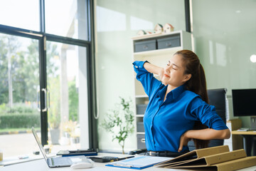 A businesswoman working at a desk in an office struggles with stress and headaches caused by Office Syndrome, a condition linked to prolonged sitting excessive computer use during long working hours