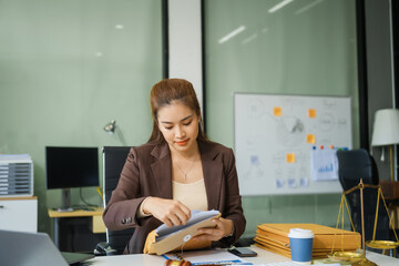 A young female lawyer sits at her desk in the office, providing online legal advice professionally. Legal documents, a computer, a judge's gavel, and scales symbolize justice and law