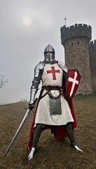 Fototapeta premium Old medieval Knights Templar warrior standing in a heroic pose. He is wearing white robes with a bold red Templar cross on his chest, over a full suit of chainmail armor