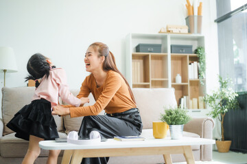 An Asian mother and her adorable daughter sit on the sofa in their living room, enjoying online...
